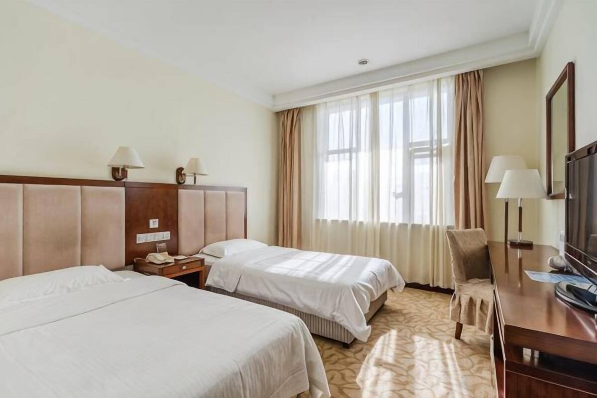 Habitación de hotel con dos camas, un escritorio, una silla y un televisor.