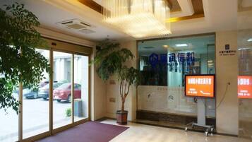 A hotel reception area with a large plant, a reception desk, and a digital screen displaying information.