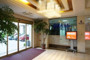 Un espace d’accueil d’hôtel comprenant une grande plante, un comptoir d’accueil et un écran numérique affichant des informations.