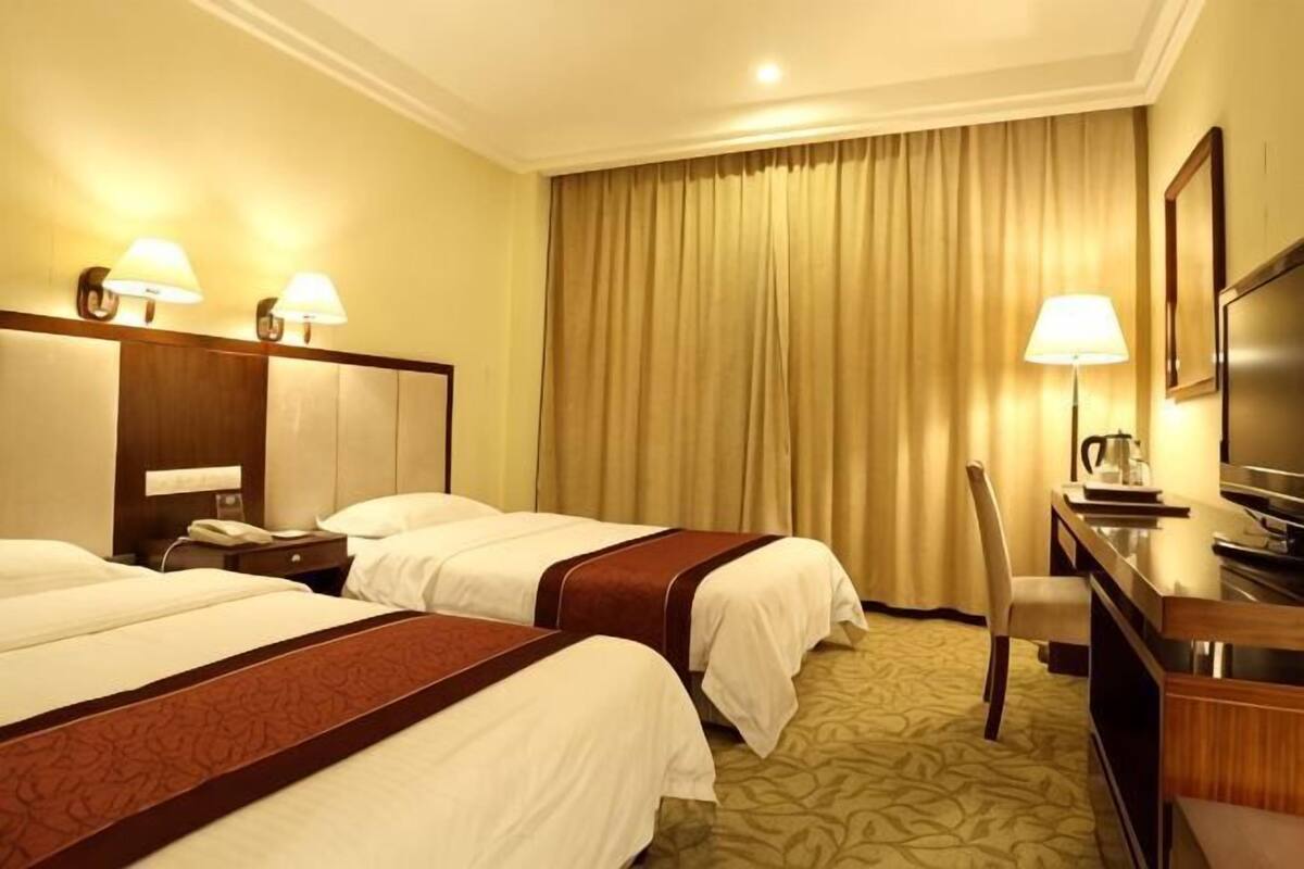 Habitación de hotel con dos camas, un escritorio, una silla, un televisor y un ventanal con cortinas.