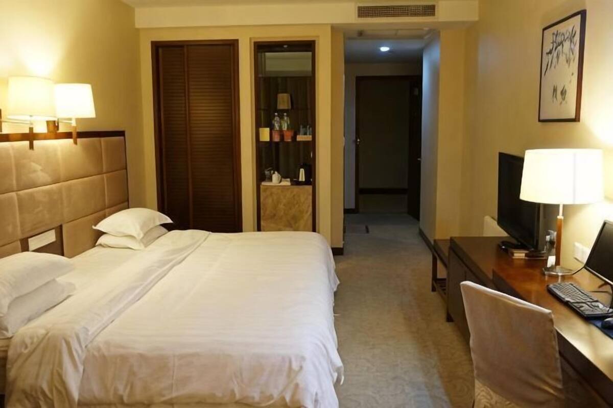 Habitación de hotel con cama, escritorio, silla, televisión y baño visible a través de una puerta abierta.