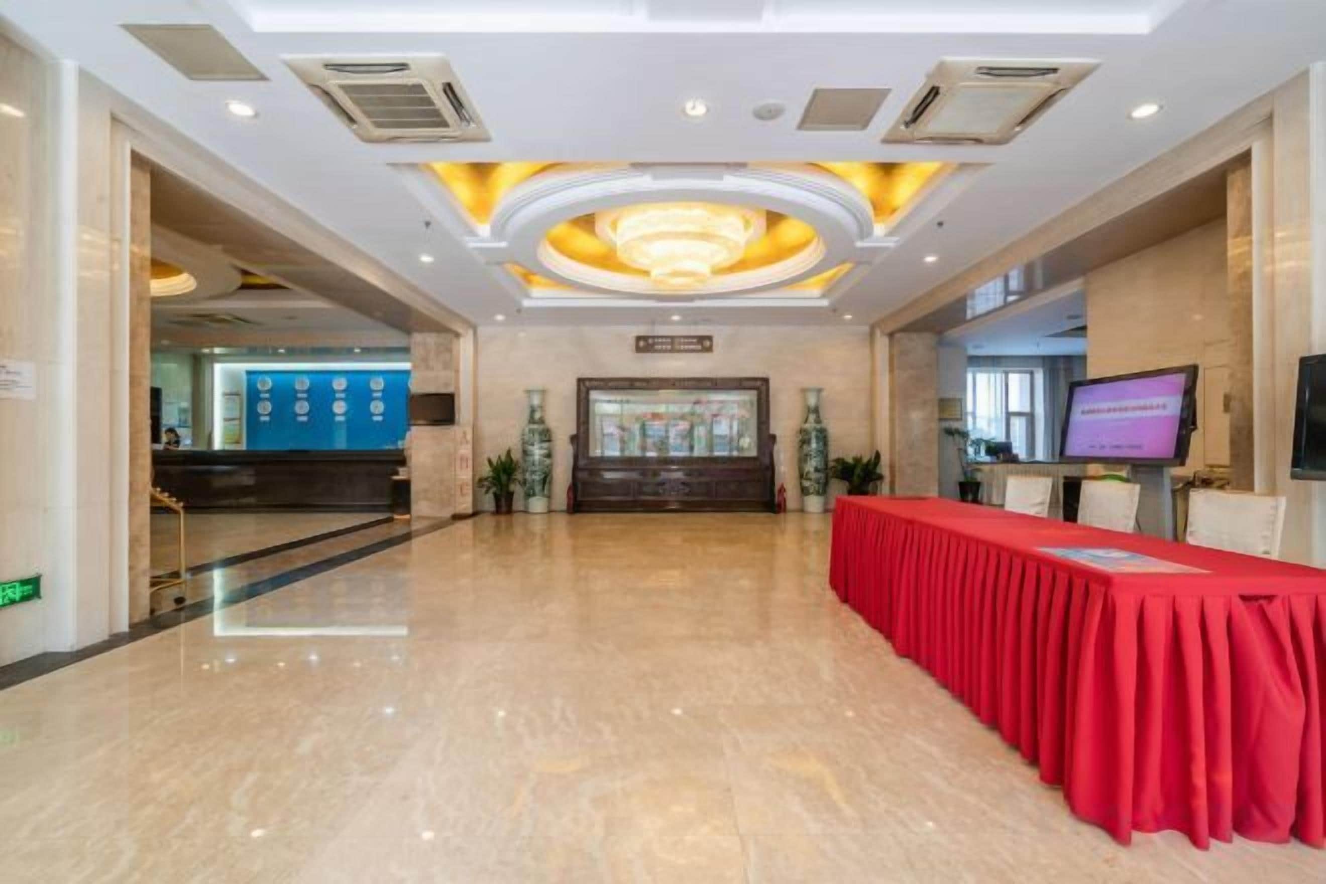 Un vestíbulo amplio con una recepción, una mesa roja y una pantalla de televisión.