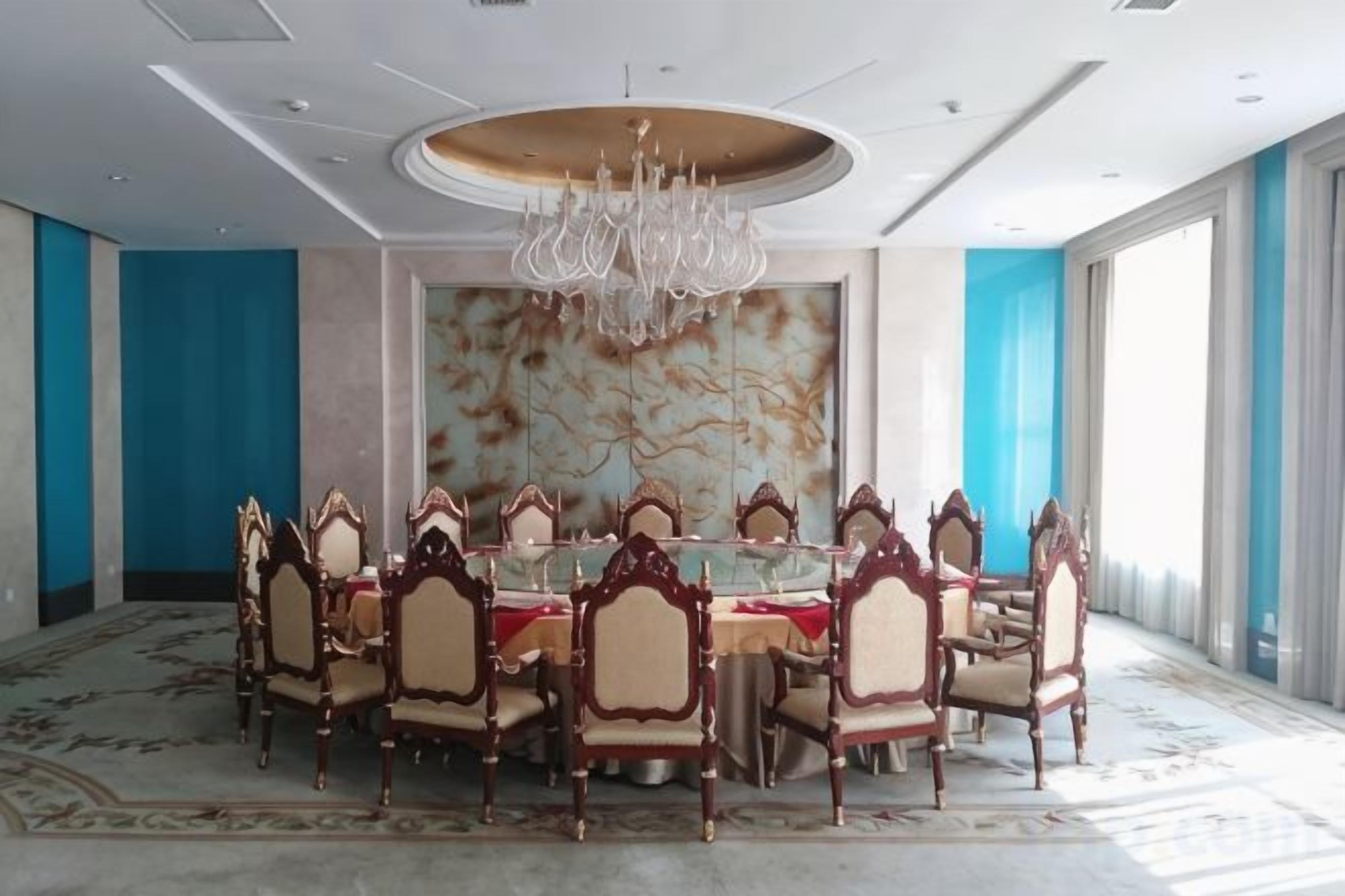 A conference room with a round table, ornate chairs, a chandelier, and large windows.