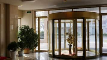 A revolving door with glass panels, a potted plant, and a red chair.