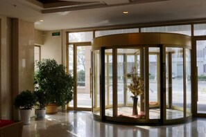 A revolving door with glass panels, a potted plant, and a red chair. - Furunge Hotel (Qingdao)