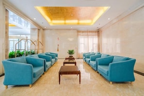 A lobby with a row of blue sofas, a wooden coffee table, and a plant in the center. - Furunge Hotel (Qingdao)