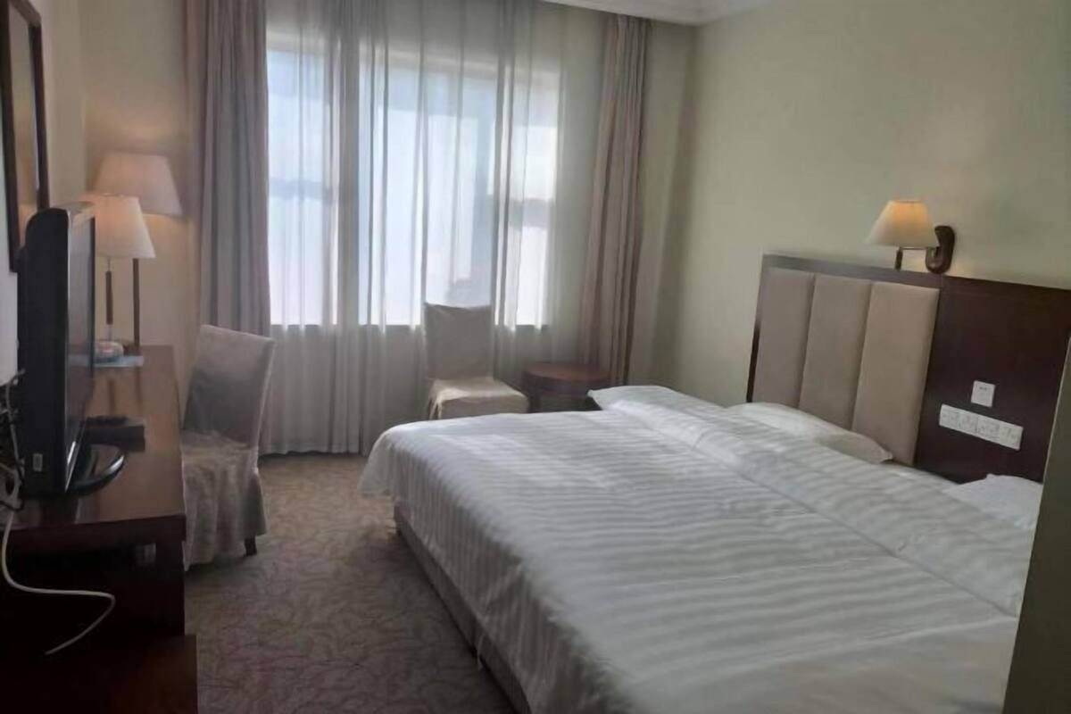 Habitación de hotel con cama, escritorio con lámpara, silla y ventana con cortinas.