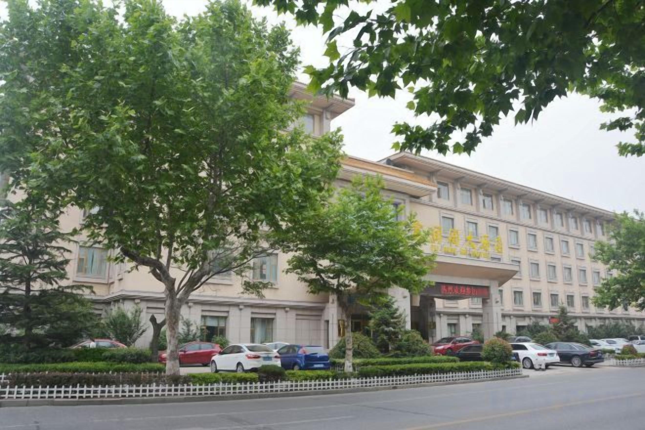 A hotel with a large building, a parking lot with several cars, and a tree in the foreground.