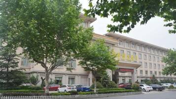 A hotel with a large building, a parking lot with several cars, and a tree in the foreground.