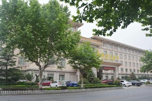 A hotel with a large building, a parking lot with several cars, and a tree in the foreground. - Furunge Hotel (Qingdao)