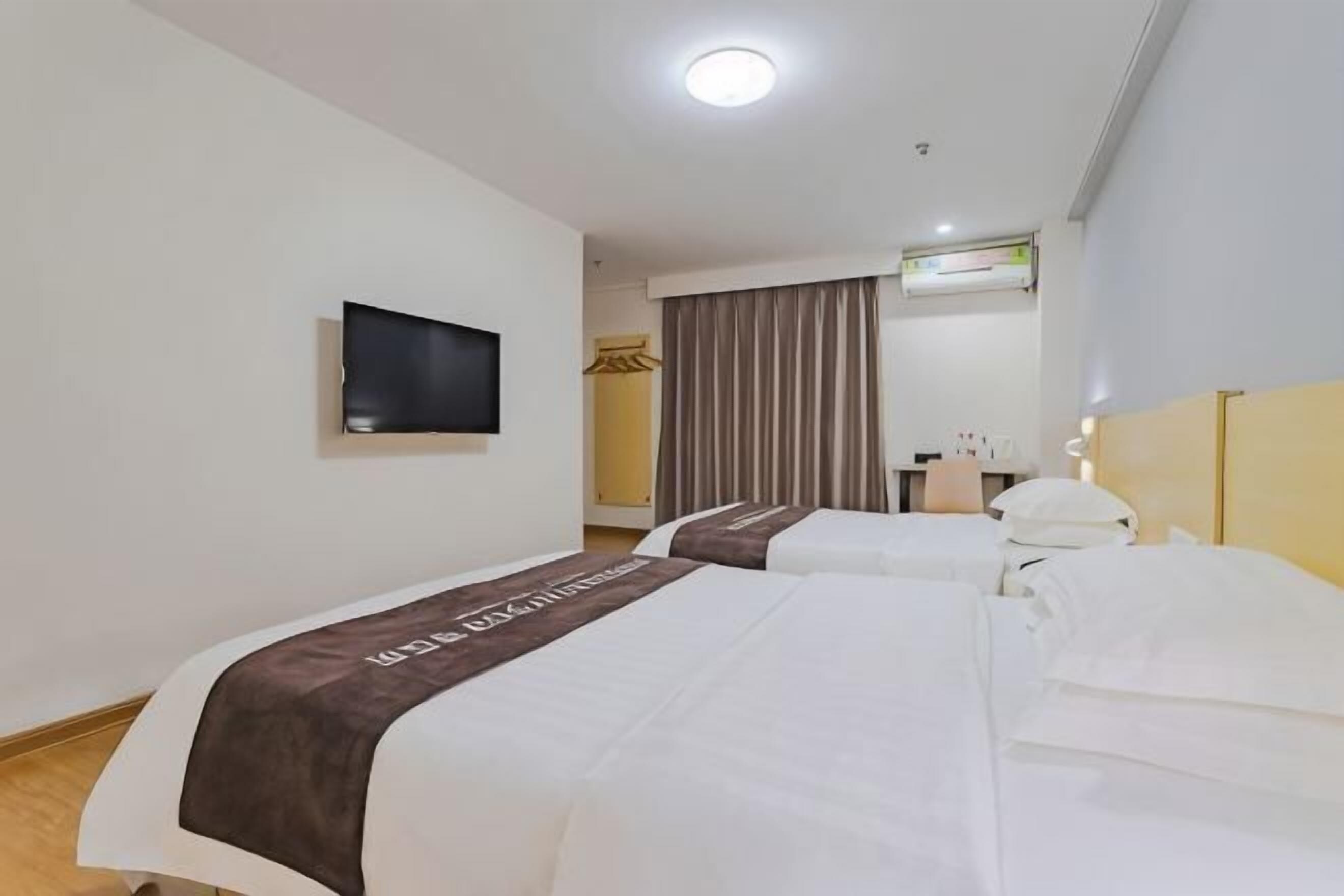A hotel room with two beds, a television, a mirror, and a window with curtains.
