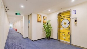 A hotel corridor with a blue carpet, a potted plant, and a yellow door with a clock and 'ONLINE STORE' sign. - Golden Season Chain Hotel (Huizhou)