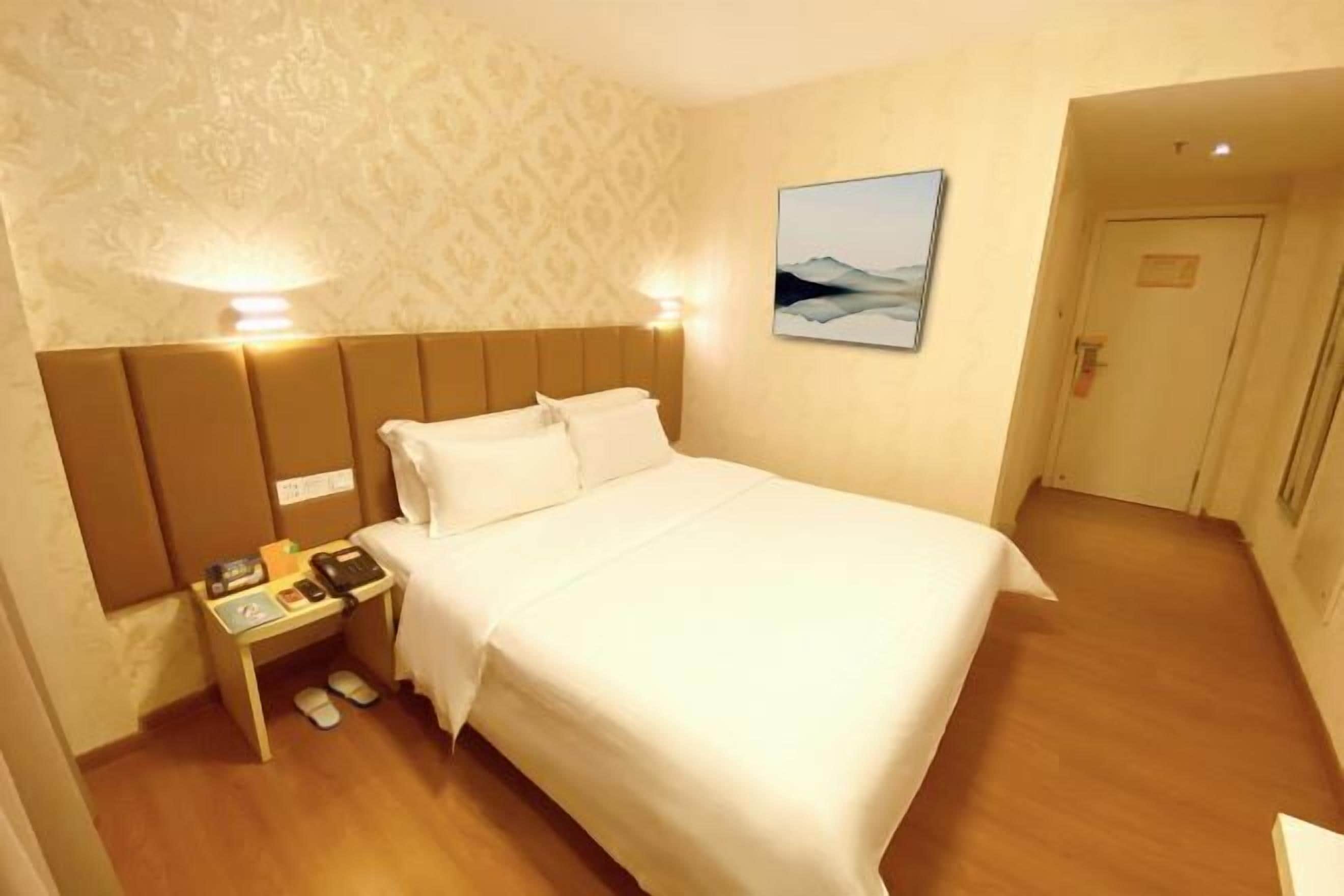 Una habitación de hotel con una cama grande, una mesita de noche con un teléfono y una lámpara, y un cuadro en la pared.