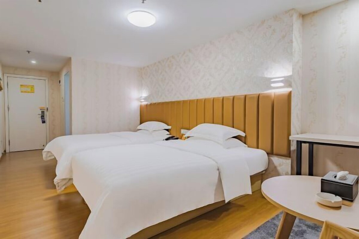 A hotel room with two beds, a wooden headboard, a small table with a phone and a box, and a door with a sign.