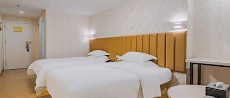A hotel room with two beds, a wooden headboard, a small table with a phone and a box, and a door with a sign.