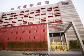 Een hotelgebouw met meerdere verdiepingen, een opvallende ingang met een glazen gevel en een kleurencombinatie van rood en wit.