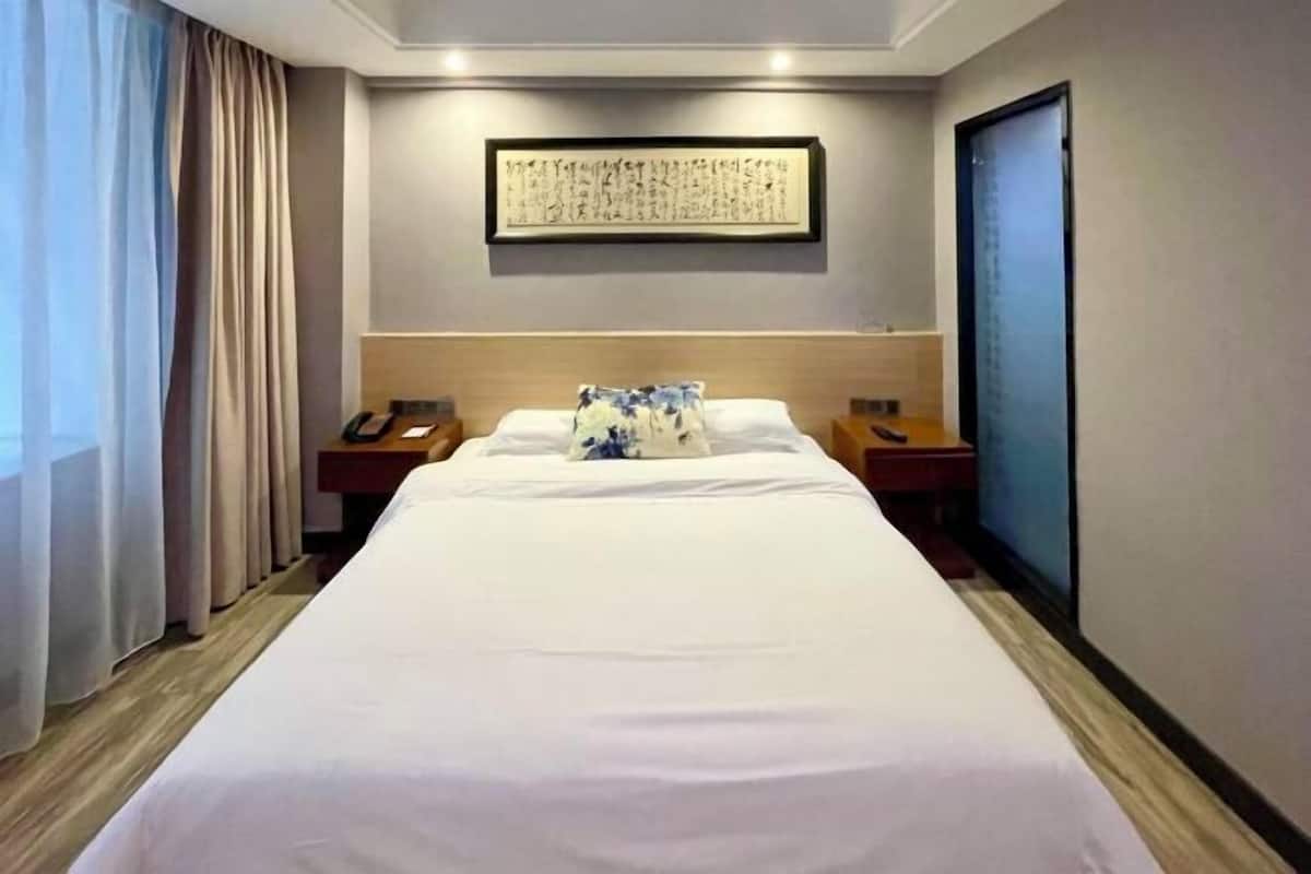 Une chambre d’hôtel avec un grand lit, des tables de chevet, un téléphone fixé au mur et une œuvre d’art encadrée au-dessus du lit.