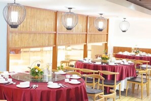 Een restaurant met ronde tafels, stoelen en hangende lampen.