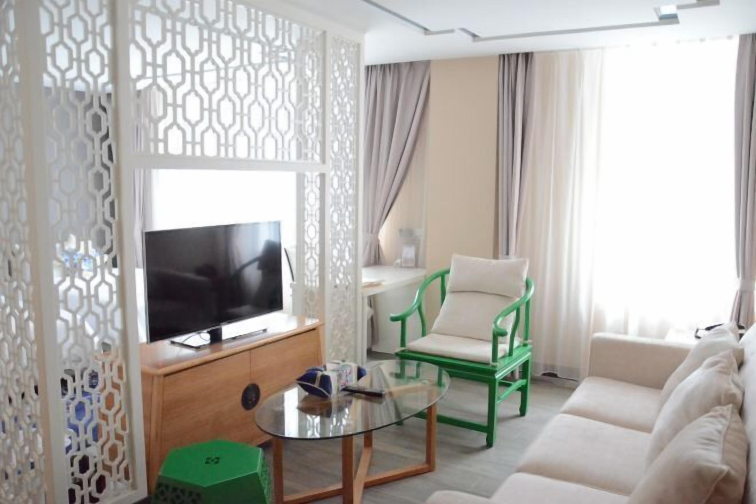 Una sala de estar moderna con un televisor de pantalla plana, una mesa de centro de vidrio, una silla verde, un sofá color beige y un panel blanco decorativo.