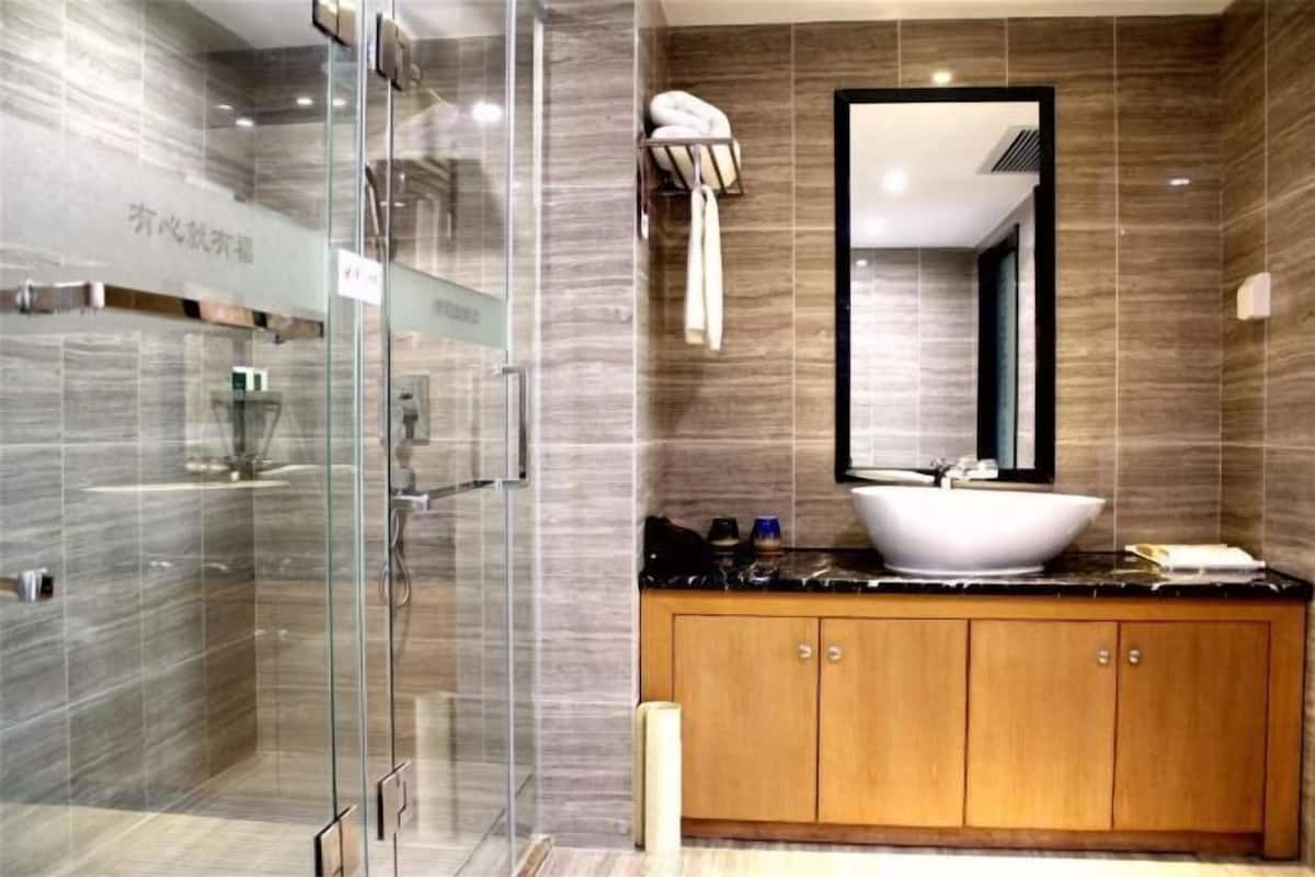 Une salle de bain moderne avec une douche à parois de verre, un meuble-lavabo en bois doté d’un grand miroir et un lavabo blanc.