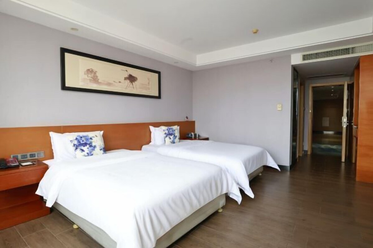 A hotel room with two beds, a nightstand, a framed picture on the wall, and a wooden floor.