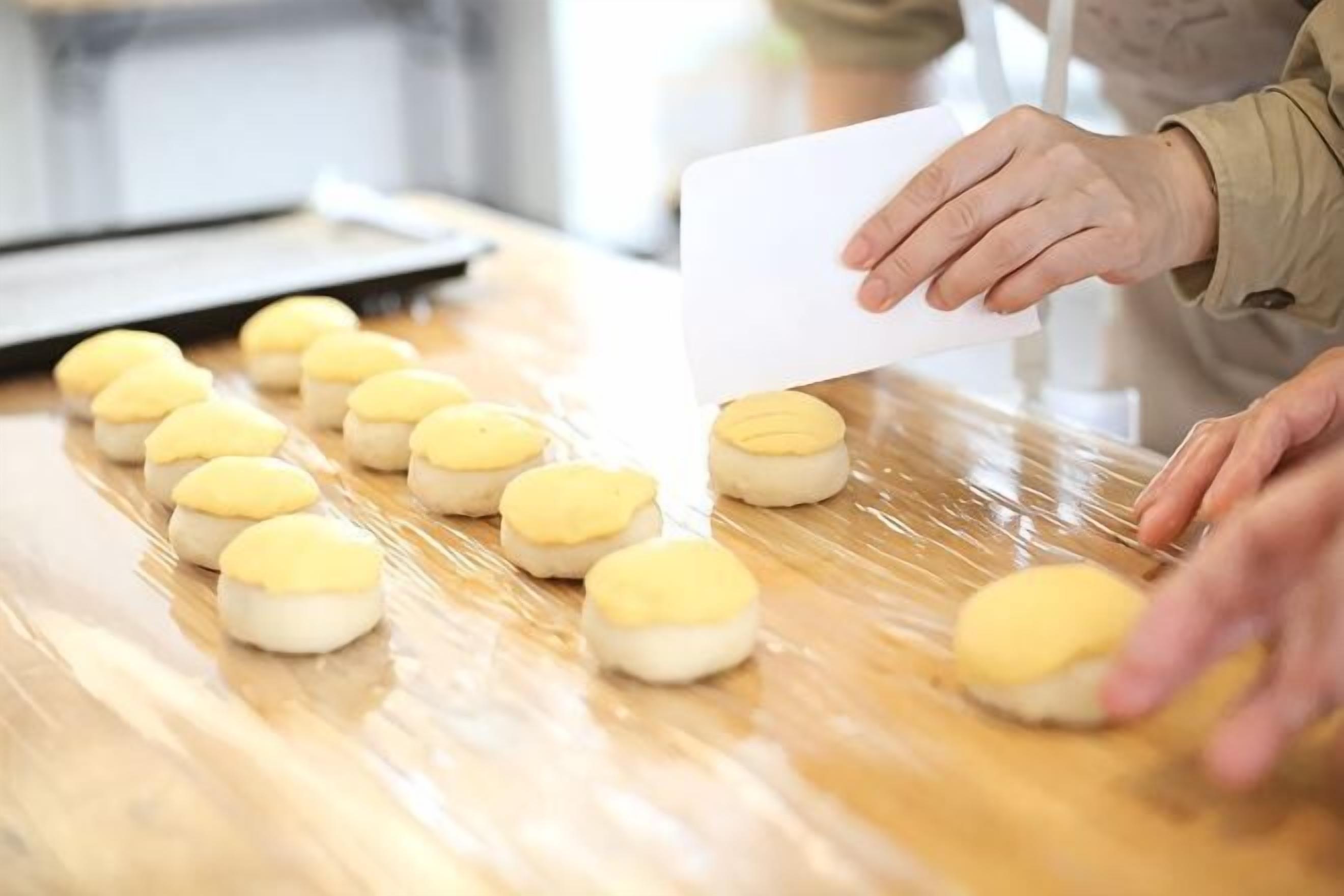 A person handling a white sheet of paper on a wooden table with several round objects, possibly food items, in a kitchen setting.