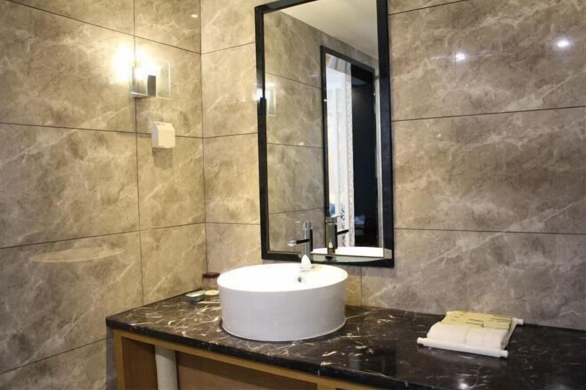 A bathroom with a marble wall, a round sink, a mirror, and a towel on the counter.