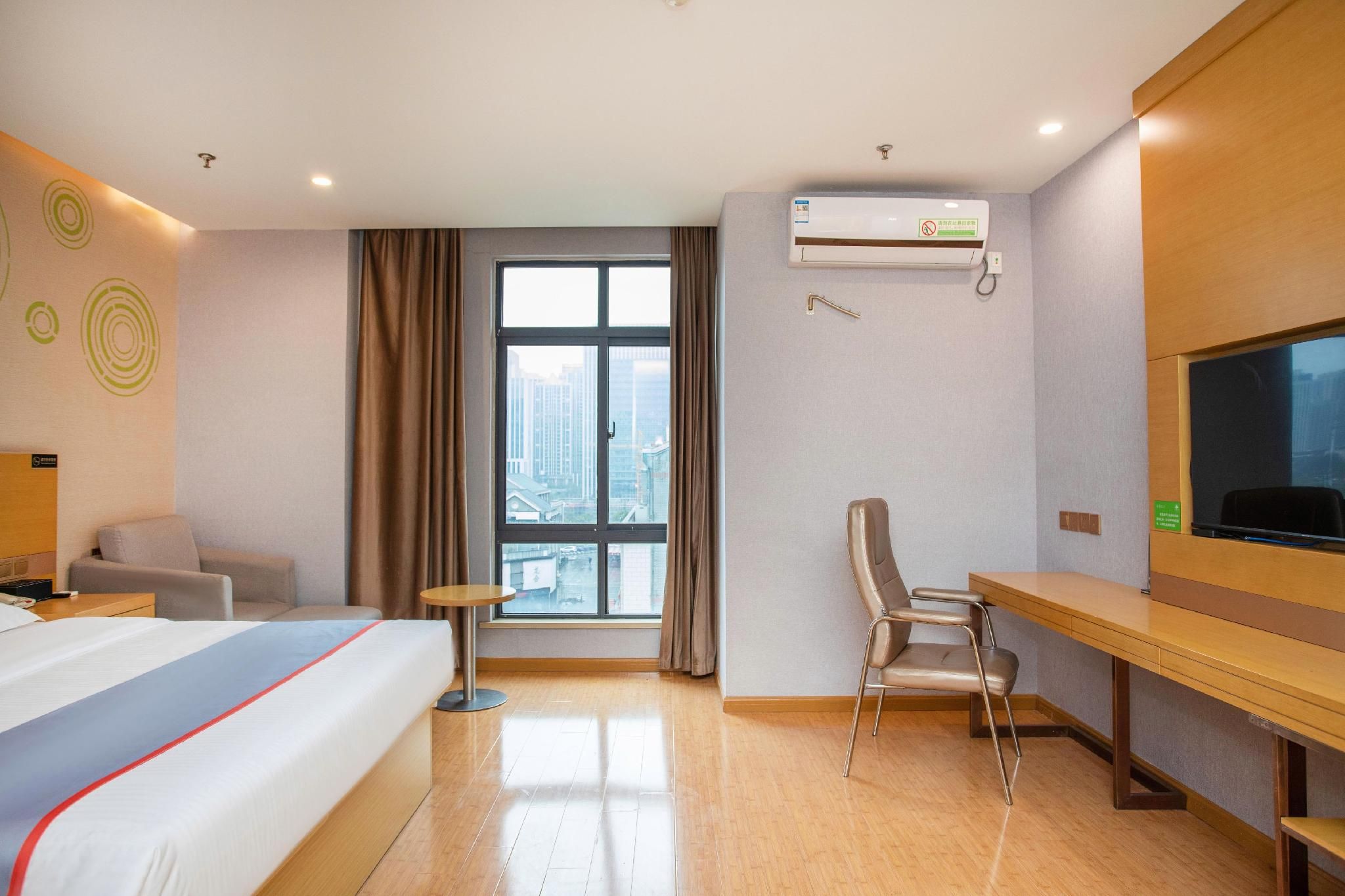 Ein Hotelzimmer mit Bett, Schreibtisch, Stuhl, Fernseher und Fenster mit Blick auf die Stadt.