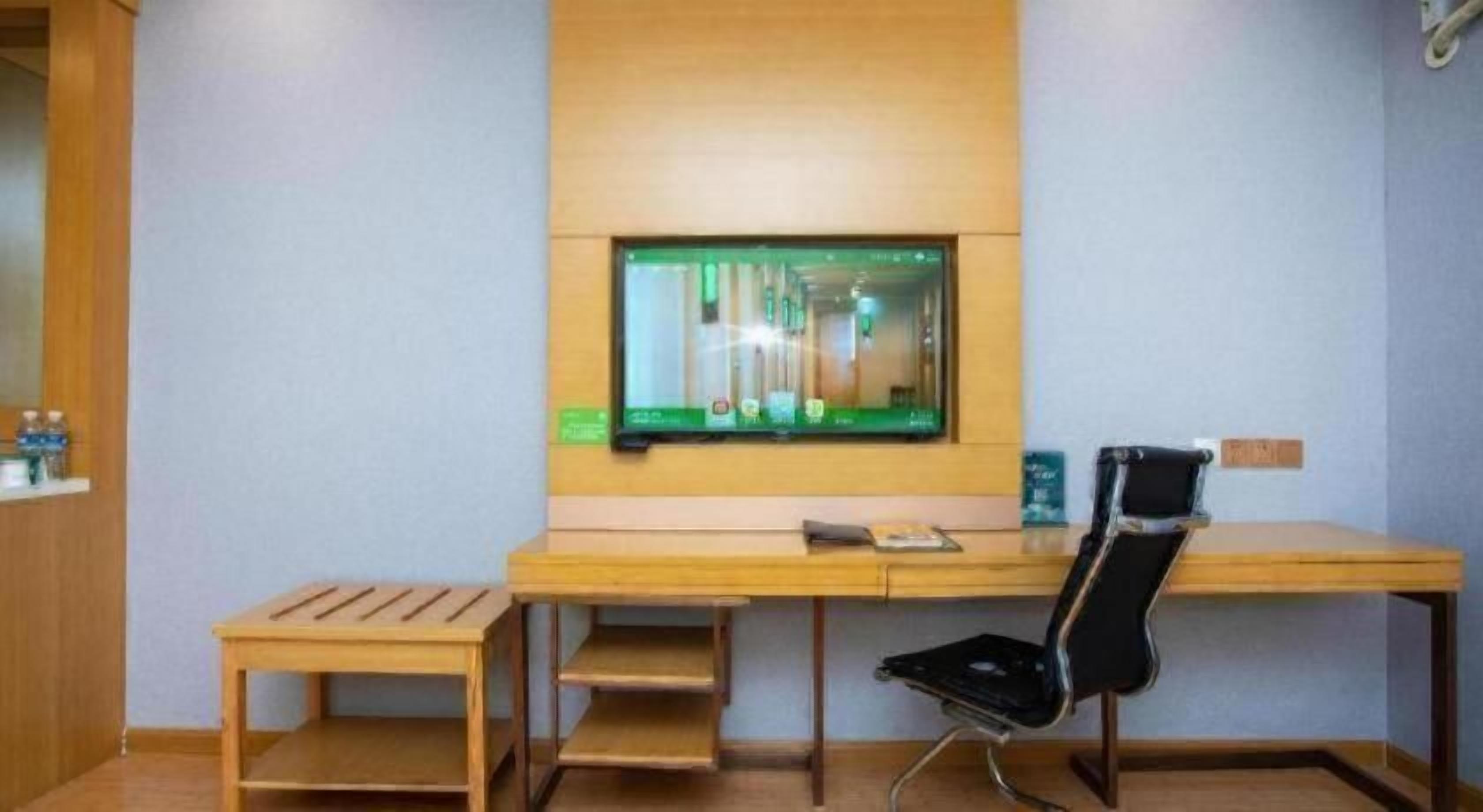 A room with a wooden desk, a black chair, and a television mounted on the wall.