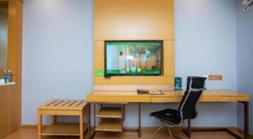 A room with a wooden desk, a black chair, and a television mounted on the wall.
