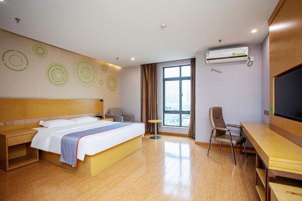 A hotel room with a bed, desk, chair, and a large window.