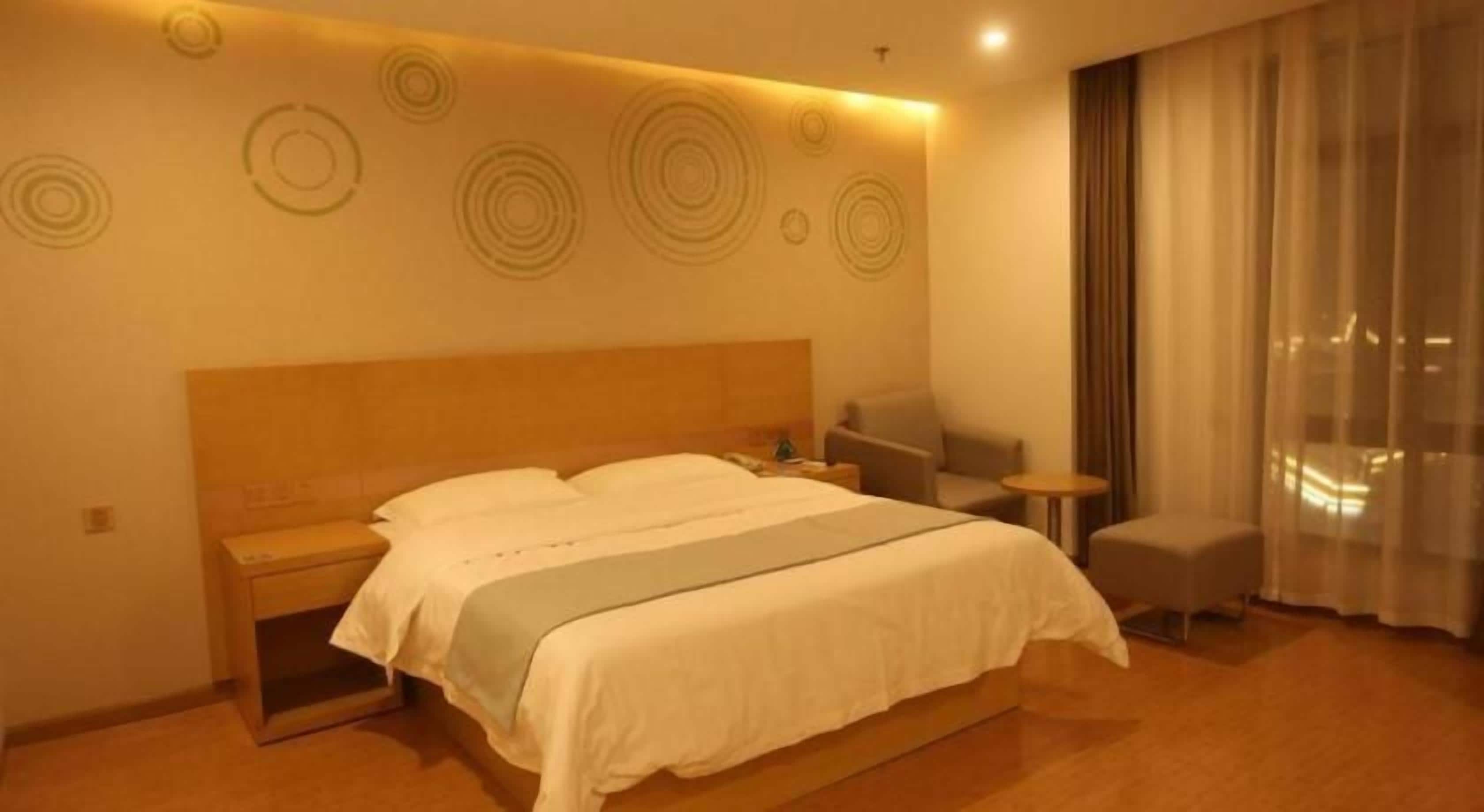 A hotel room with a large bed, bedside tables, a chair, and a view of the city through the window.