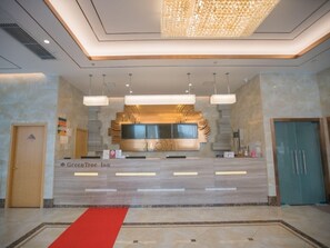 Een hotel receptie met een marmeren balie, een rood tapijt en een moderne kroonluchter.