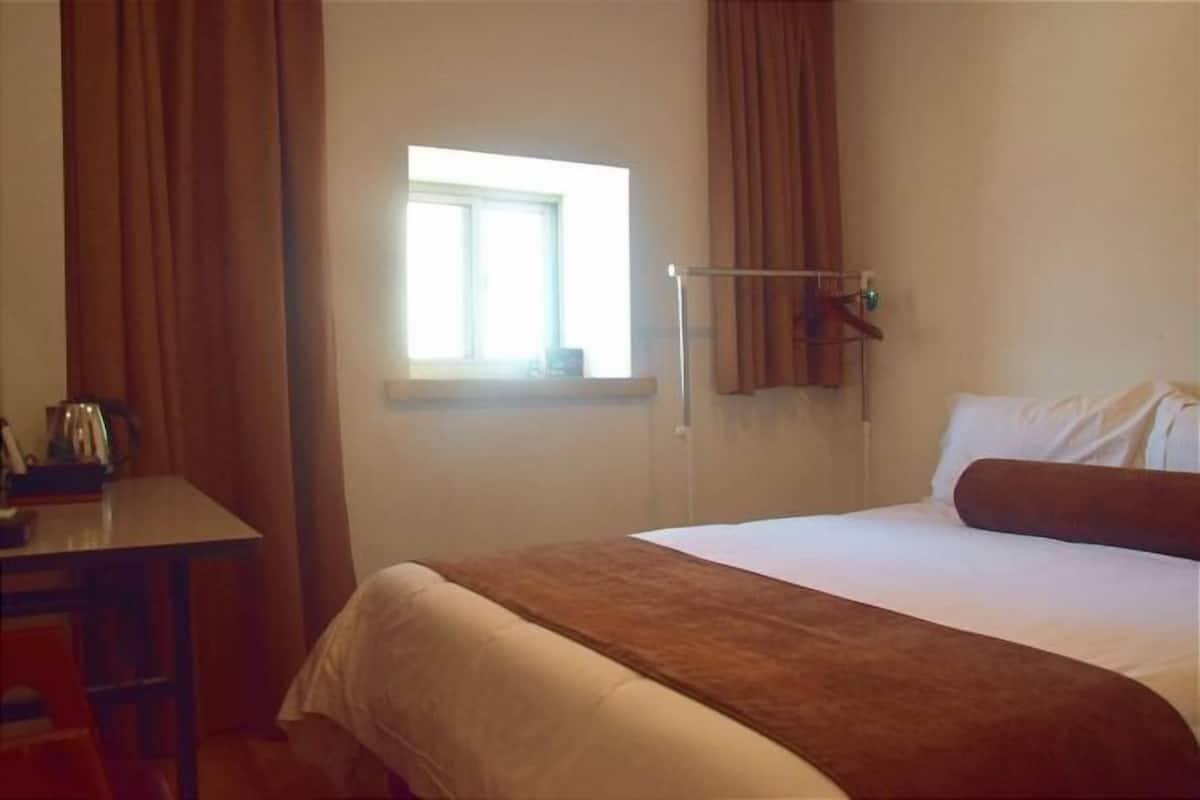 Une chambre d’hôtel avec un lit, un bureau, une fenêtre et des rideaux.