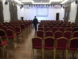 A conference room with rows of red chairs, a podium, and a screen at the front. - S One Hotel (Shanghai)