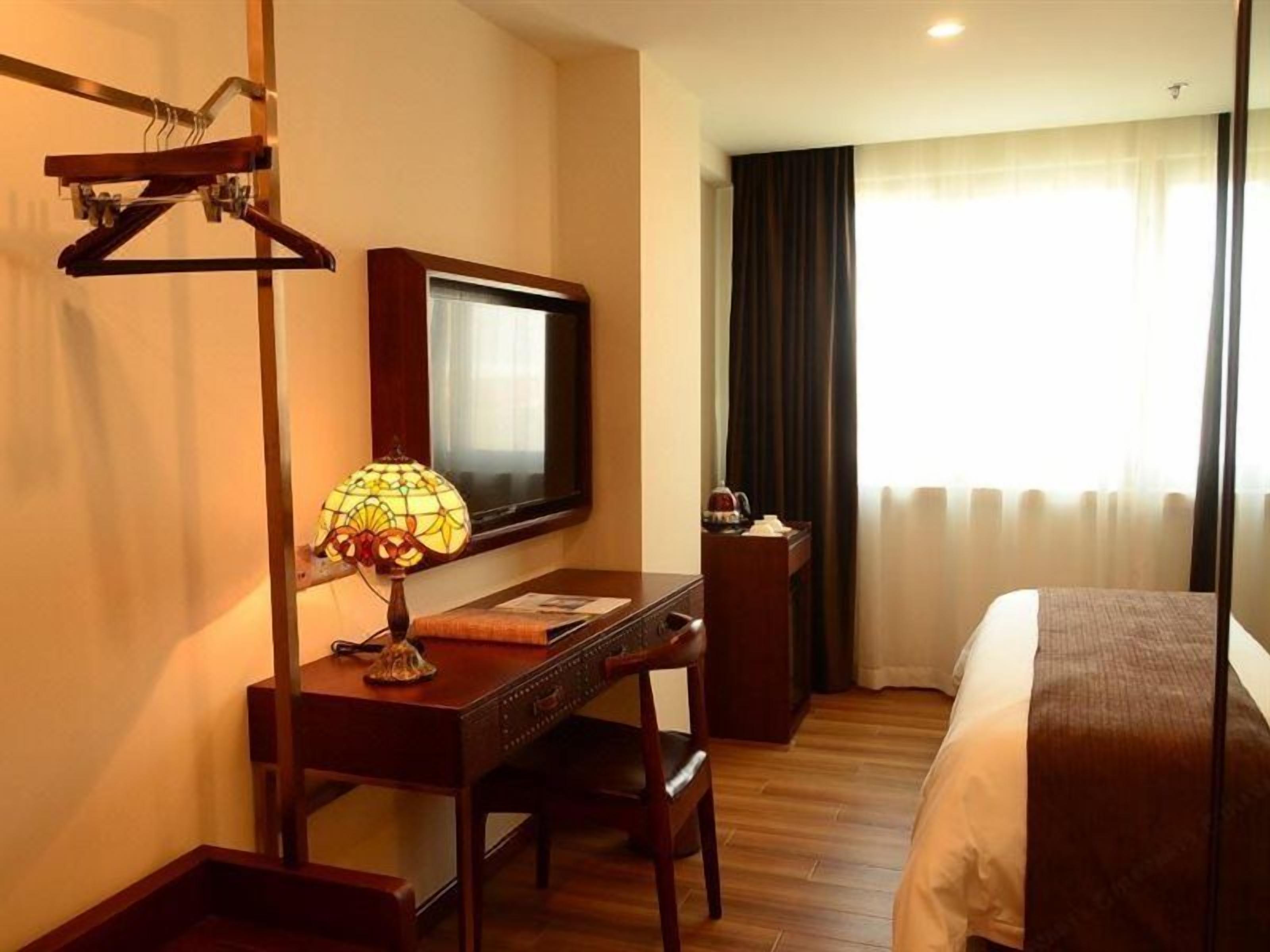 Habitación de hotel con cama, escritorio con lámpara, televisión y ventana con cortinas.