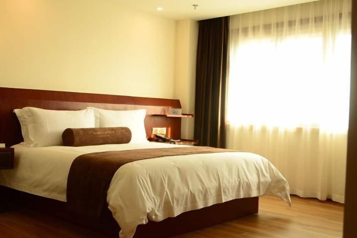 Une chambre d’hôtel avec un grand lit, une table de chevet et une fenêtre avec des rideaux.
