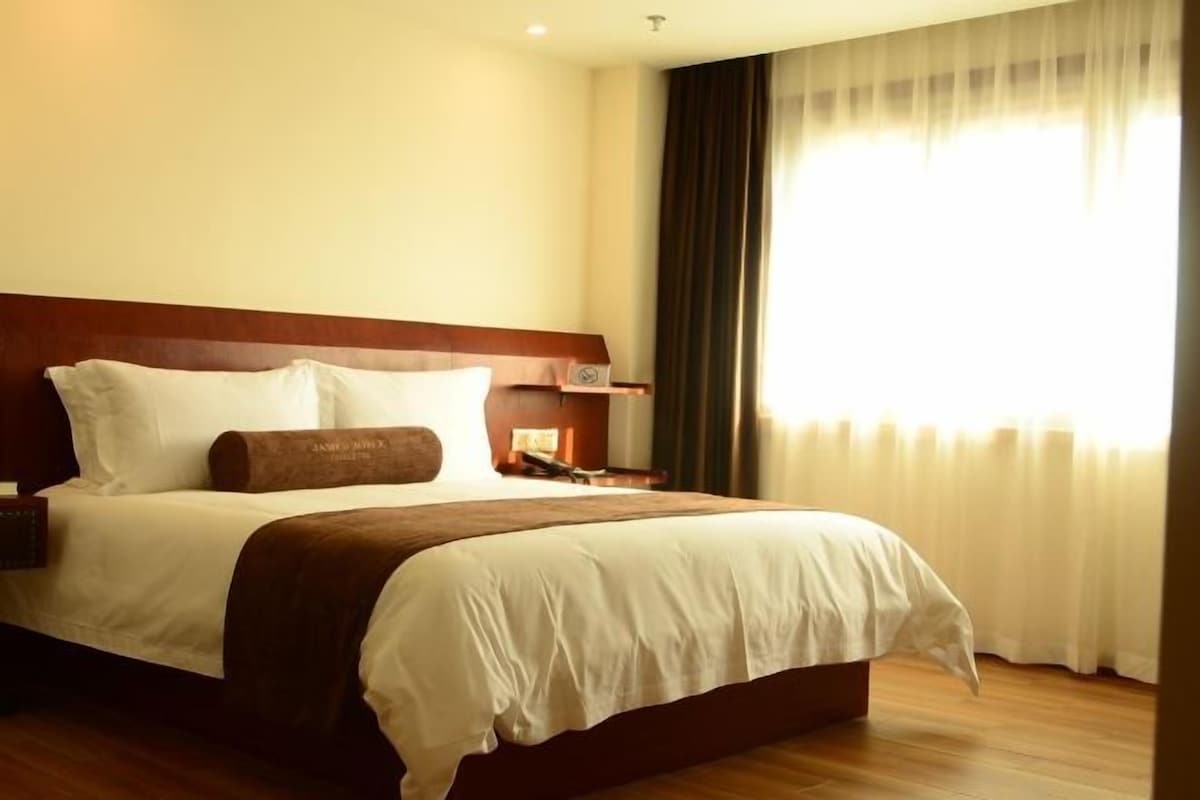 A hotel room with a large bed, a nightstand, and a window with curtains.
