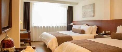A hotel room with two beds, a desk with a lamp, and a window with curtains.