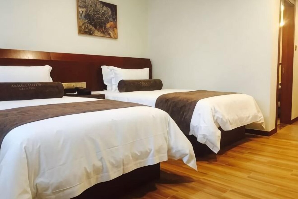 A hotel room with two beds, wooden flooring, a nightstand, and a painting on the wall.