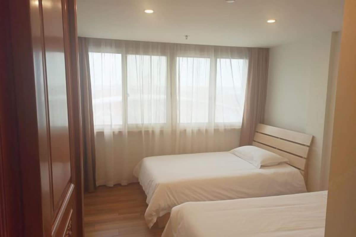A bedroom with two single beds, a wooden headboard, and a large window with sheer curtains.