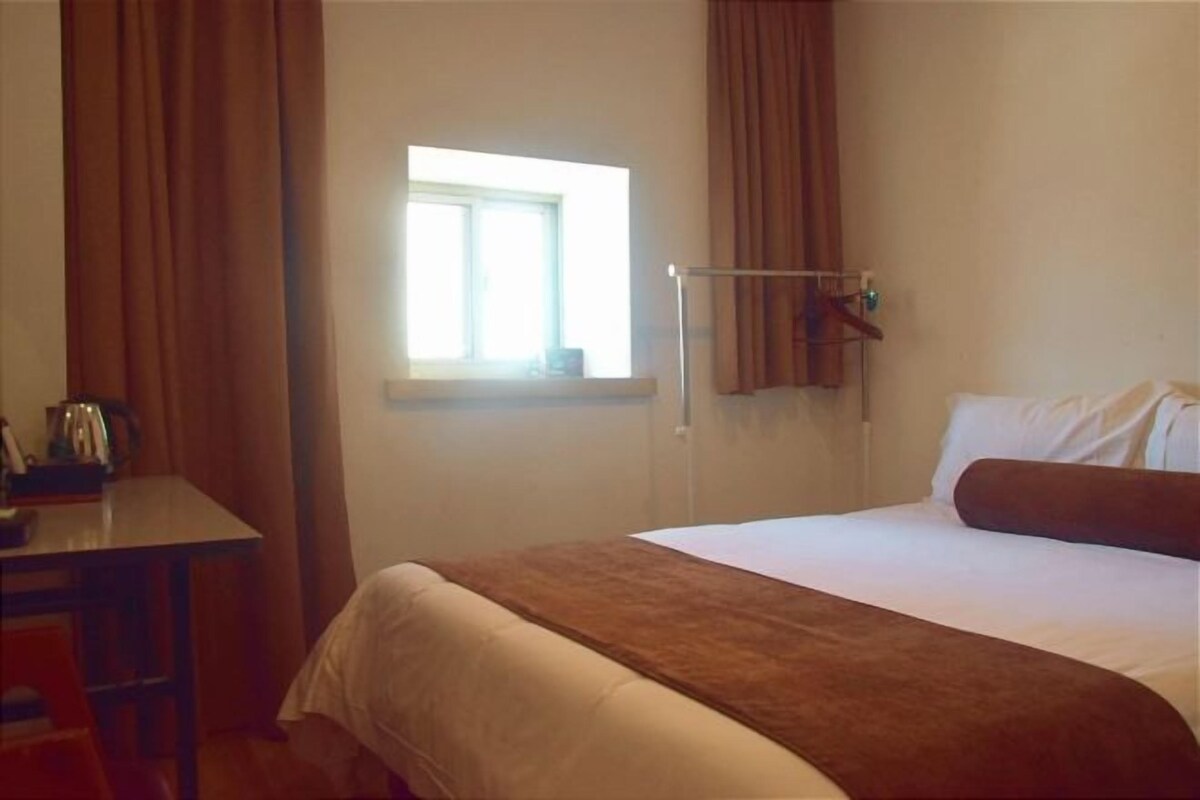 A hotel room with a bed, a desk, a window, and curtains.