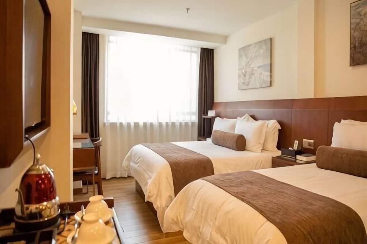 Une chambre d’hôtel avec deux lits, un bureau, une chaise, une lampe et une vue sur l’extérieur.