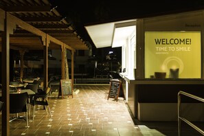An outdoor restaurant area with a reception desk, a chalkboard menu, and tables and chairs. - Coral Dreams (Adeje)