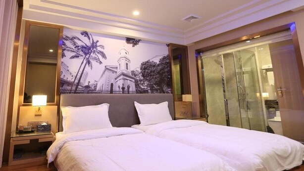 A hotel room with a large bed, a nightstand with a lamp, a glass shower enclosure, and a mural of a church and palm trees on the wall. - Chonpines Hotel (Guangzhou)