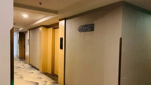 A hotel corridor with a patterned carpet, doors, and a sign indicating a room or area. - Chonpines Hotel (Guangzhou)