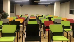 A conference room with rows of chairs in various colors, a projector screen at the front, and a plant in the corner. - Chonpines Hotel (Guangzhou)