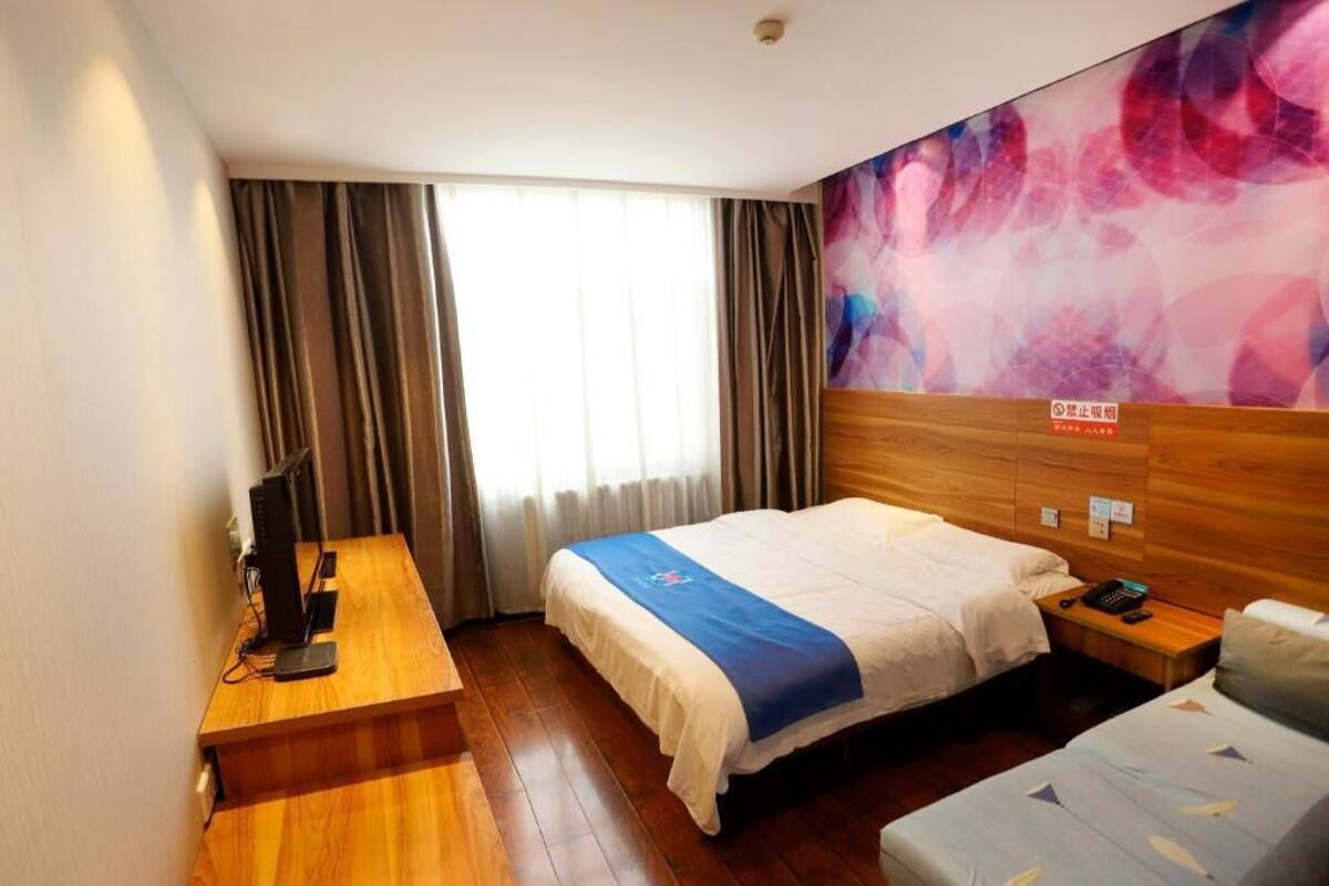 Habitación de hotel con cama, escritorio con computadora, silla, mesita de noche con teléfono y un cuadro abstracto grande en la pared.