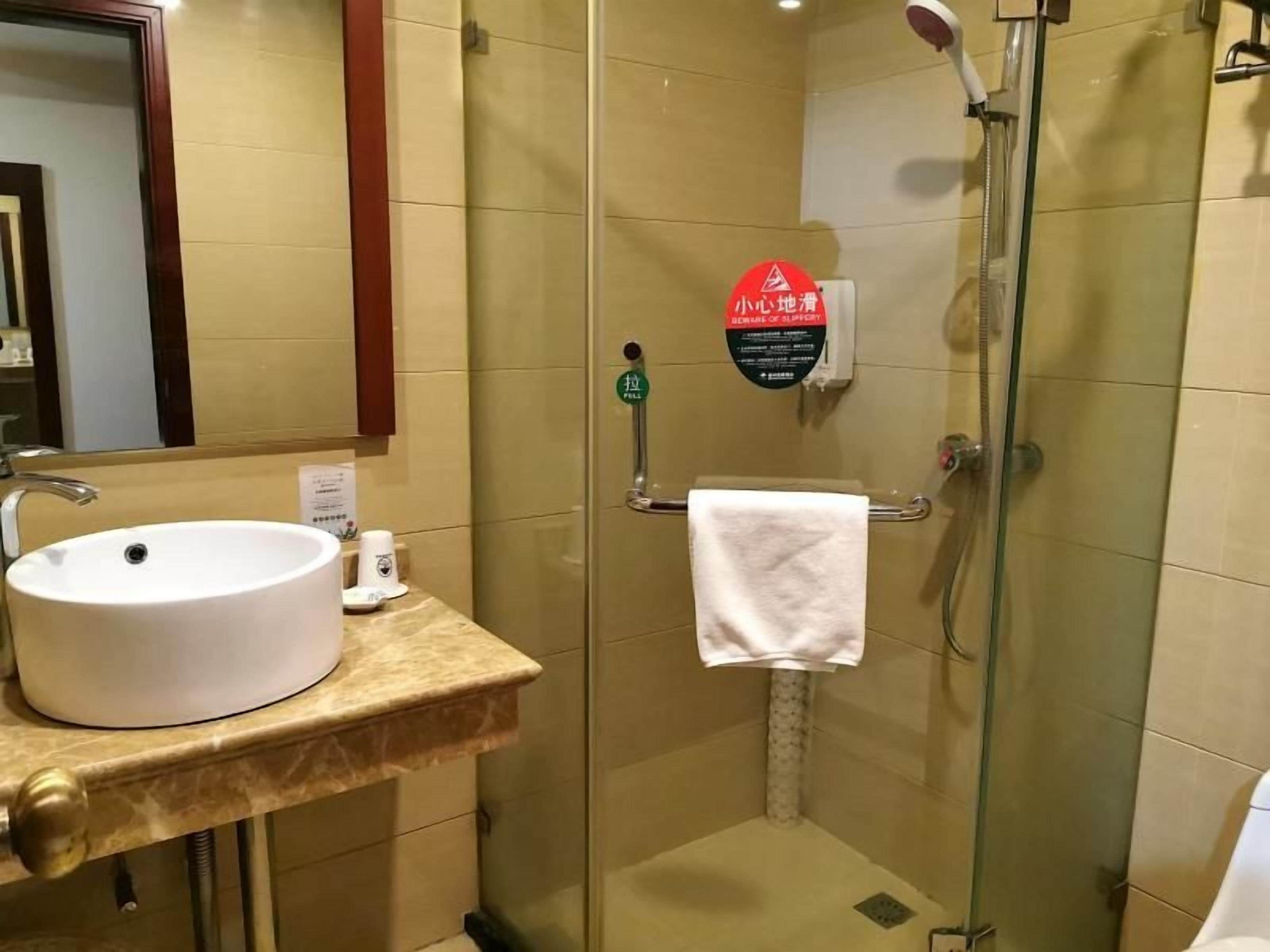 Ett hotellbadrum med handfat, en duschkabin med glasväggar och en handduksställning.