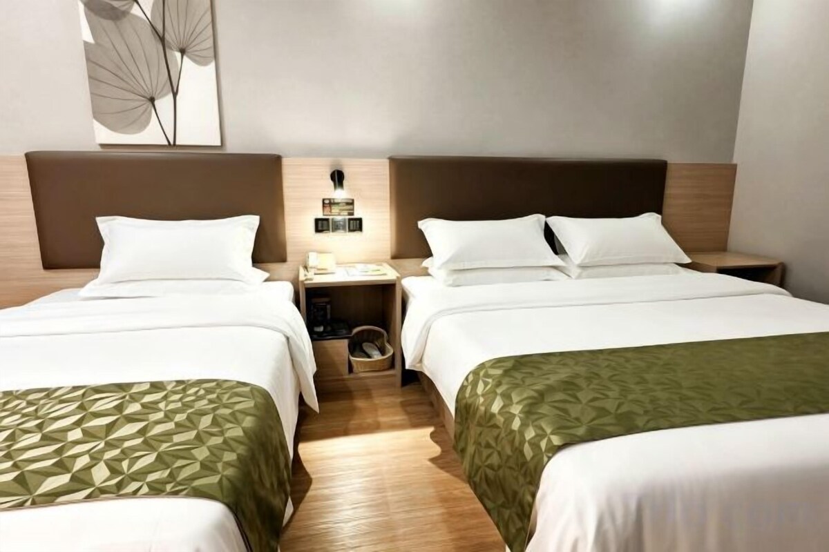 Ein Hotelzimmer mit zwei Einzelbetten, einem Nachttisch mit Lampe und einer Wandleuchte.